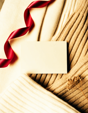 Buono regalo XO Boutique appoggiato su maglieria piegata color crema